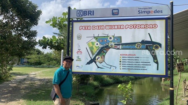 Kepala BUMDes Potorono, Sutardi, berdiri di depan peta desa wisata. (Suara.com/Irwan Febri)