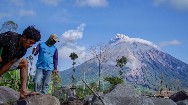 Dua warga beraktivitas dengan latar belakang Gunung Semeru mengeluarkan asap vulkanis, di Desa Supiturang, Lumajang, Jawa Timur, Senin (20/4/2026). [ANTARA FOTO/Irfan Sumanjaya/kye]