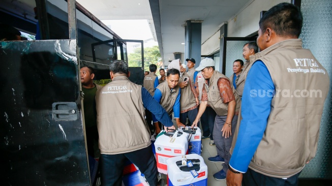 Petugas menyusun koper calon jamaah haji kedalam bus di Asrama Haji Pondok Gede, Jakarta, Selasa (21/4/2026). [Suara.com/Alfian Winanto]
