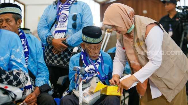 Petugas membantu calon jamaah haji yang memasuki Asrama Haji Pondok Gede, Jakarta, Selasa (21/4/2026). [Suara.com/Alfian Winanto]
