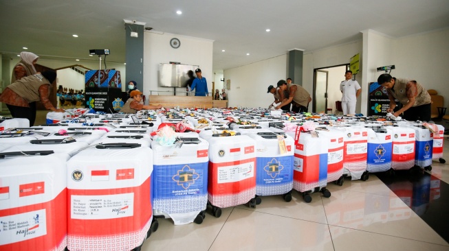 Petugas menyusun koper calon jamaah haji yang memasuki Asrama Haji Pondok Gede, Jakarta, Selasa (21/4/2026). [Suara.com/Alfian Winanto]
