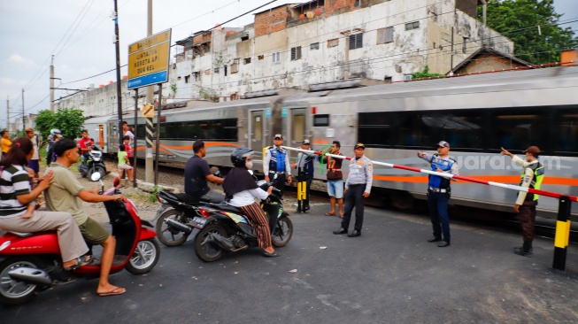 Pengendara berhentinsaat kereta melintas di perlintasan kereta api di dekat Stasiun Bekasi Timur, Bekasi, Jawa Barat, Rabu (30/4/2026). [Suara.com/Alfian Winanto]
