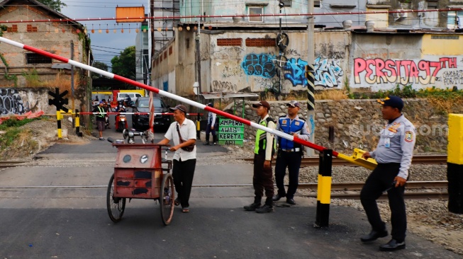 Pedagang melintasi rel perlintasan kereta api di dekat Stasiun Bekasi Timur, Bekasi, Jawa Barat, Rabu (30/4/2026). [Suara.com/Alfian Winanto]
