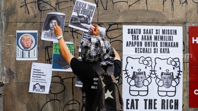 Massa dari berbagai elemen masyarakat dan buruh menempelkan poster pada aksi memperingati Hari Buruh Internasional atau May Day 2026 di depan gedung DPR RI, Jakarta, Jumat (1/5/2026). [Suara.com/Alfian Winanto]
