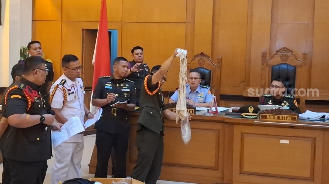 Oditur militer menunjukkan barang bukti pakaian dan kacamata milik korban yang rusak parah akibat siraman air keras, Rabu (6/5/2026). (Suara.com/Yoga)