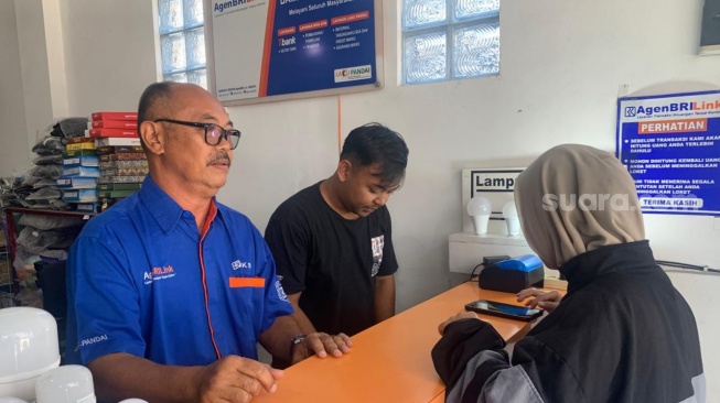 Pemilik agen BRILink, Bambang Margono, saat melayani kosumen di tokonya. (Suara.com/Irwan Febri)