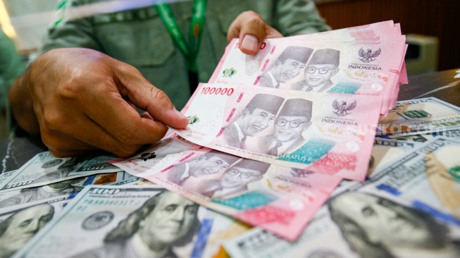 Petugas salah satu tempat penukaran mata uang asing menunjukkan uang rupiah dan dollar AS di Jakarta, Selasa (19/5/2026). [Suara.com/Alfian Winanto]
