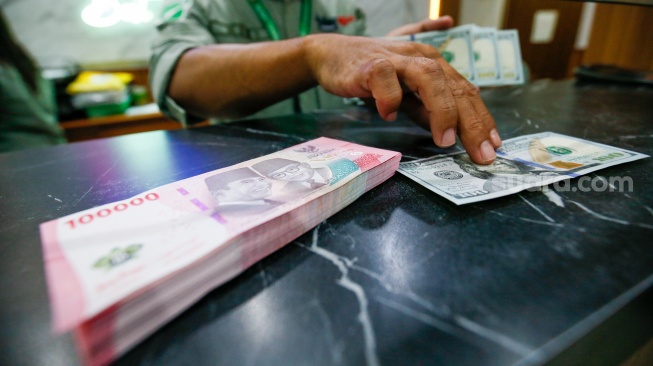Petugas salah satu tempat penukaran mata uang asing menunjukkan uang rupiah dan dollar AS di Jakarta, Selasa (19/5/2026). [Suara.com/Alfian Winanto]