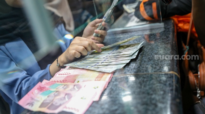 Petugas salah satu tempat penukaran mata uang asing menunjukkan uang rupiah dan dollar AS di Jakarta, Selasa (19/5/2026). [Suara.com/Alfian Winanto]