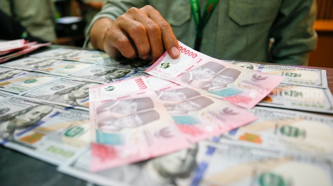 Petugas salah satu tempat penukaran mata uang asing menunjukkan uang rupiah dan dollar AS di Jakarta, Selasa (19/5/2026). [Suara.com/Alfian Winanto]
