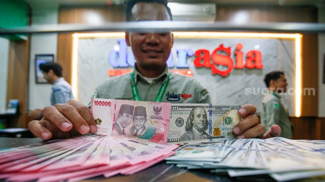 Petugas salah satu tempat penukaran mata uang asing menunjukkan uang rupiah dan dollar AS di Jakarta, Selasa (19/5/2026). [Suara.com/Alfian Winanto]