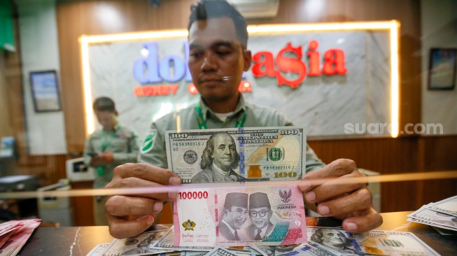 Petugas salah satu tempat penukaran mata uang asing menunjukkan uang rupiah dan dollar AS di Jakarta, Selasa (19/5/2026). [Suara.com/Alfian Winanto]