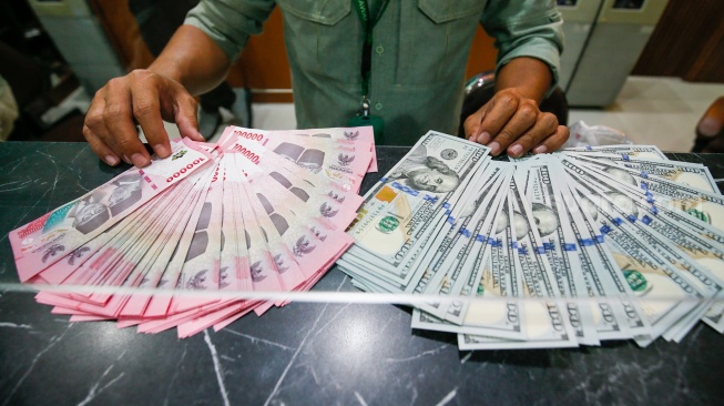 Petugas salah satu tempat penukaran mata uang asing menunjukkan uang rupiah dan dollar AS di Jakarta, Selasa (19/5/2026). [Suara.com/Alfian Winanto]