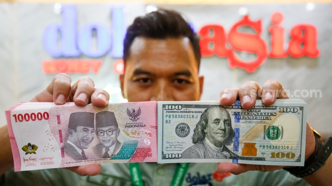 Petugas salah satu tempat penukaran mata uang asing menunjukkan uang rupiah dan dollar AS di Jakarta, Selasa (19/5/2026). [Suara.com/Alfian Winanto]