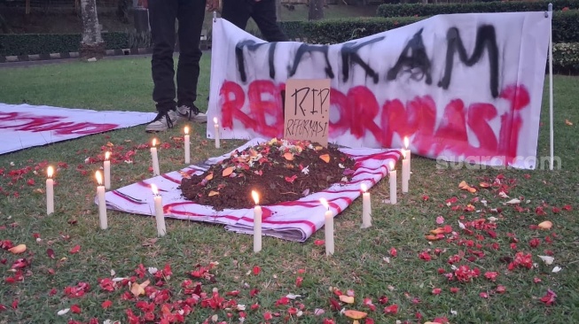 Sebuah peragaan berbentuk makam dengan batu nisan yang terbuat dari kardus bertuliskan "R.I.P REFORMASI" dalam aksi massa "#Reformati" di Tugu Makara UI, Universitas Indonesia, Depok, Rabu (20/5/2026). (Suara.com/Cornelius Juan Prawira)