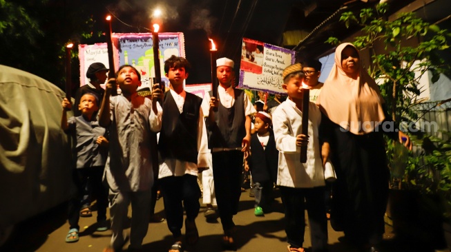 Sejumlah warga dan anak-anak mengikuti pawai obor di Kawasan Menteng, Jakarta Pusat, Senin (15/6/2026).  [Suara.com/Alfian Winanto]