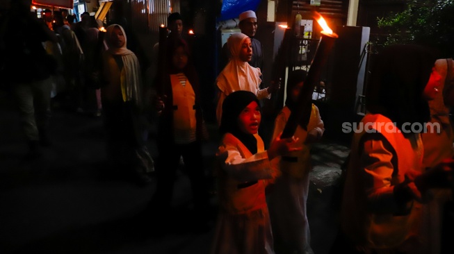Sejumlah warga dan anak-anak mengikuti pawai obor di Kawasan Menteng, Jakarta Pusat, Senin (15/6/2026).  [Suara.com/Alfian Winanto]