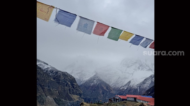 Bendera doa berwarna-warni berkibar di atas pos peristirahatan pendaki dengan latar belakang puncak gunung bersalju di Nepal, Jumat (29/5/2026). [Suara.com/Rizka Chaerani] 