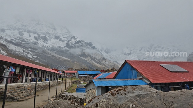 Seorang pendaki berjalan di area penginapan dengan latar belakang dinding es berselimut kabut di jalur trekking Annapurna Base Camp, Nepal, Jumat (29/5/2026). [Suara.com/Rizka Chaerani] 