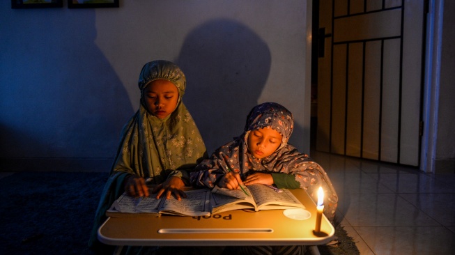 IESR menyatakan bahwa krisis pasokan batubara domestik menyebabkan pemadaman listrik bergilir di sejumlah wilayah Indonesia. Foto: Dua orang anak di Kabupaten Bandung, Jawa Barat sedang mengaji menggunakan penerangan lilin akibat pemadaman bergilir pada Juni 2026. [Antara]