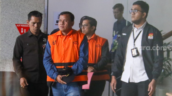 Bupati Kuantan Singingi Suhardiman Amby (tengah) berjalan menuju mobil tahanan usai menjalani pemeriksaan di Gedung Merah Putih KPK, Jakarta, Rabu (1/7/2026). [Suara.com/Alfian Winanto]
