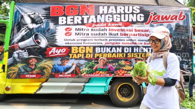 Warga membawa sayuran yang dibagikan massa aksi saat berunjuk rasa mendukung program MBG di Jakarta, Rabu (8/7/2026). [Suara.com/Alfian Winanto]
