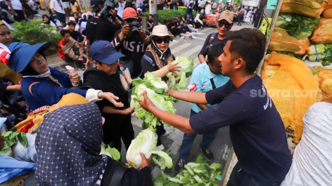 Massa aksi membagikan sayuran kepada warga saat berunjuk rasa mendukung program MBG di Jakarta, Rabu (8/7/2026). [Suara.com/Alfian Winanto]