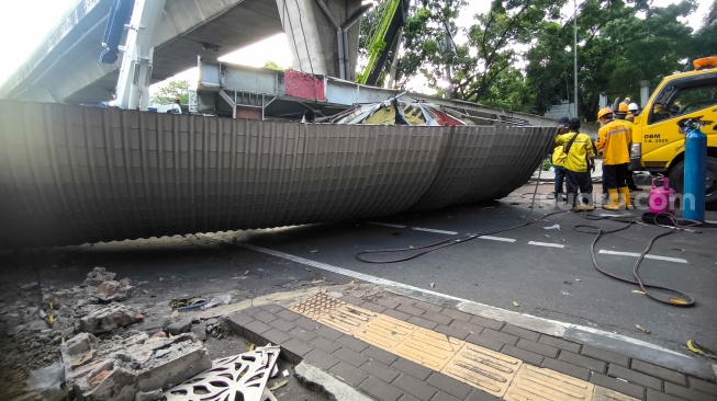 Petugas membongkar Jembatan Penyeberangan Orang (JPO) Tendean yang rusak usai tertabrak truk pengangkut alat berat di kawasan Tendean, Jakarta, Selasa (14/7/2026). [Suara.com/Alfian Winanto]