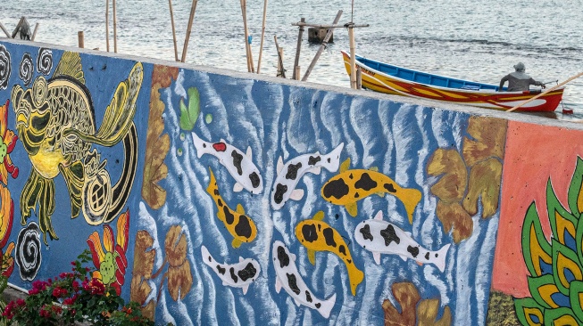 Nelayan menggunakan perahu melintas di dekat tanggul pengaman pantai yang dihiasi mural bertema lingkungan di Kampung Bahari Tambaklorok, Semarang, Jawa Tengah, Kamis (23/7/2026). [ANTARA FOTO/Aprillio Akbar/foc]