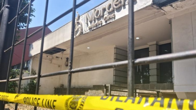 Suasana depan Mordent Aesthetic Clinic, Senin, Kebayoran Baru, Jakarta, Senin (27/7/2026). Garis polisi terpasang di pagar hitam serta pintu masuk kaca klinik. (Suara.com/Juan)
