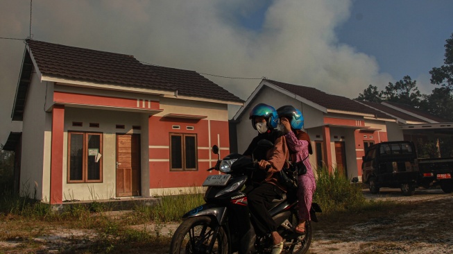 Warga melintas dengan latar belakang kepulan asap akibat kebakaran lahan di kawasan permukiman Tegal Sari, Palangka Raya, Kalimantan Tengah, Jumat, (7/8/2026). [ANTARA FOTO/Auliya Rahman/hma]
