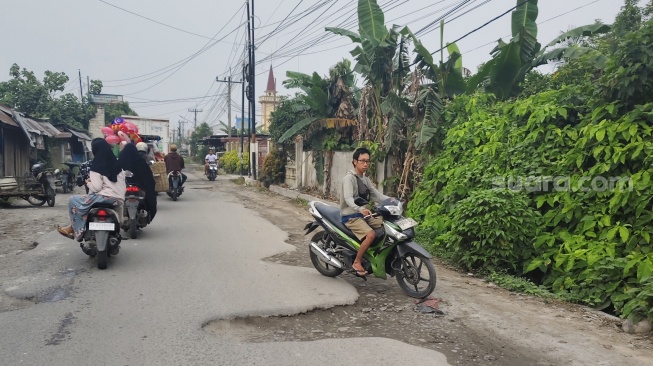 Warga melewati jalan rusak di Jalan Glugur Rimbun-Diski, di Kecamatan Sunggal, Deli Serdang. [Suara.com/ M.Aribowo]