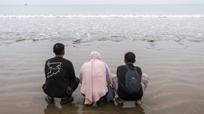 Istri dan anak jurnalis Merdeka.com yang hilang kontak, Arie Basuki, Yanti (tengah) dan Bintang (kanan) berdoa sebelum melakukan tabur bunga di bibir Pantai Kampung Pagedongan, Carita, Pandeglang, Banten, Jumat (18/9/2026). [ANTARA FOTO/Angga Budhiyanto/agr]