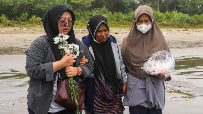 Istri dan ibu jurnalis ANTARA yang hilang kontak, M Bagus Khoirunas, Desi Purnama Sari (kiri) dan Tini (tengah) berdoa usai melakukan tabur bunga di bibir Pantai Kampung Pagedongan, Carita, Pandeglang, Banten, Jumat (18/9/2026). [ANTARA FOTO/Angga Budhiyanto/agr]