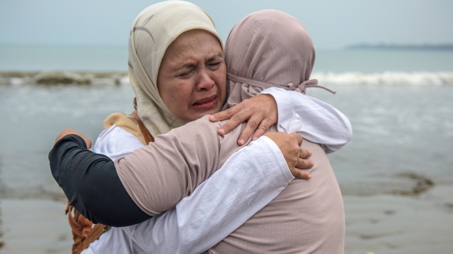 Istri Arie Basuki, Yanti (kanan) berpelukan dengan kakak dari Arie Basuki, Dewi saat melakukan tabur bunga di pantai Pagedongan, Pandeglang, Banten, Jumat (18/9/2026). [ANTARA FOTO/Paramayuda/agr]