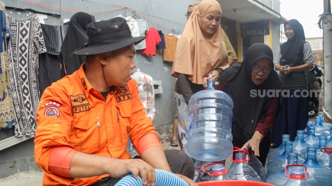 Personel BPBD Jakarta Selatan mengisi air ke dalam wadah milik warga yang terdampak kekeringan di Lenteng Agung, Jakarta, Jumat (18/9/2026). [Suara.com/Alfian Winanto]