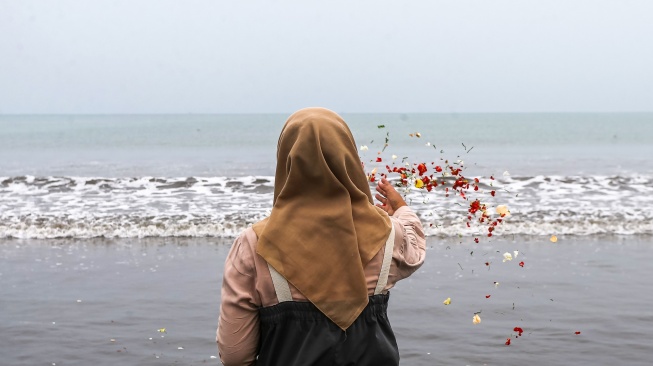Seorang jurnalis melakukan tabur bunga di bibir Pantai Kampung Pagedongan, Carita, Pandeglang, Banten, Jumat (18/9/2026). [ANTARA FOTO/Angga Budhiyanto/agr]