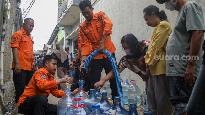 Personel BPBD Jakarta Selatan mengisi air ke dalam wadah milik warga yang terdampak kekeringan di Lenteng Agung, Jakarta, Jumat (18/9/2026). [Suara.com/Alfian Winanto]