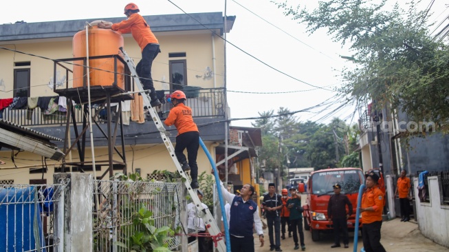 Personel BPBD Jakarta Selatan mengisi air ke dalam wadah milik warga yang terdampak kekeringan di Lenteng Agung, Jakarta, Jumat (18/9/2026). [Suara.com/Alfian Winanto]