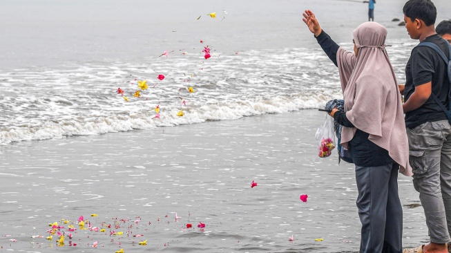 Istri Arie Basuki Yanti (kiri) menabur bunga didampingi Bintang di pantai Pagedongan, Pandeglang, Banten, Jumat (18/9/2026). [ANTARA FOTO/Paramayuda/agr]
