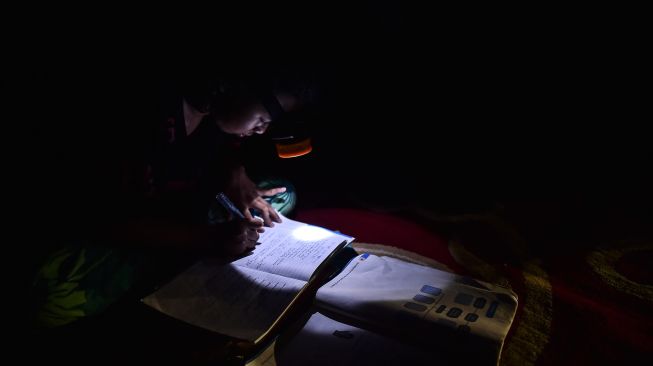 Seorang pelajar belajar dengan penerangan lampu senter di dalam rumahnya yang belum mendapatkan layanan listrik di Dusun Suka Jaya, Desa Lagan Ulu, Tanjung Jabung Timur, Jambi, Rabu (7/10/2026). [ANTARA FOTO/Wahdi Septiawan/wsj]
