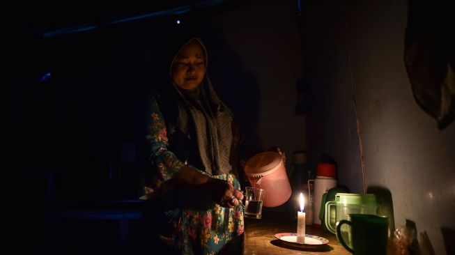 Seorang warga menuangkan air ke dalam gelas dengan penerangan lilin di dalam rumahnya yang belum mendapatkan layanan listrik di Dusun Suka Jaya, Desa Lagan Ulu, Tanjung Jabung Timur, Jambi, Rabu (7/10/2026). [ANTARA FOTO/Wahdi Septiawan/wsj]