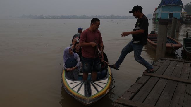 Tiga warga duduk di perahu motor di Sungai Kapuas yang diselimuti kabut asap pekat di Pontianak, Kalimantan Barat, Kamis (8/10/2026). [ANTARA FOTO/Jessica Wuysang/ky]