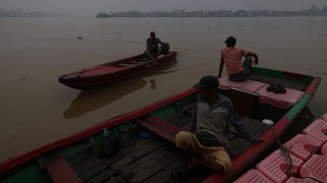 Tiga warga duduk di perahu motor di Sungai Kapuas yang diselimuti kabut asap pekat di Pontianak, Kalimantan Barat, Kamis (8/10/2026). [ANTARA FOTO/Jessica Wuysang/ky]