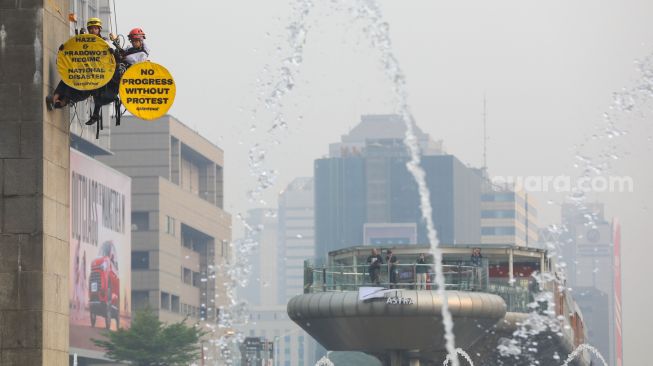 Sejumlah aktifis Greenpeace membentangkan spanduk yang bertema krisis iklim di Bundaran HI, Jakarta, Selasa (20/10/2026). [Suara.com/Alfian Winanto]
