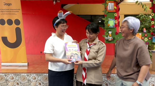 Quality Assurance Specialist Bank Jago Hana Simanjuntak (dari kiri) secara simbolis  menyerahkan donasi buku Jagoan Baca kepada Kepala Sekolah SDN 10 Mekarjaya Viptri didampingi Employee Engagement & People Partner Lead Bank Jago Fitri Dianasari  saat acara roadshow edukasi literasi keuangan dan minat baca melalui program Jagoan Baca di Depok, Jawa Barat, Rabu (21/10/2026). [Handout]