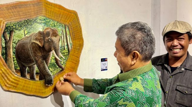 Seorang pengunjung menandai lukisan yang dibelinya di pameran tunggal Utopia karya Yohanes Fitri di Galeri Hang Nadim (GHN), Anjungan Kampar Kompleks Bandar Serai Pekanbaru, Rabu (21/10/2026) malam. [Ist]
