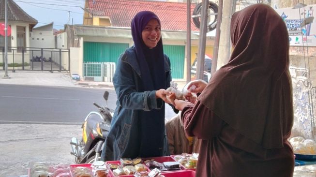 Firdhailsa Cintora, pedagang makanan ringan saat mengirim barang jualannya di warung jajanan pasar. [Suara.com/Baktora]