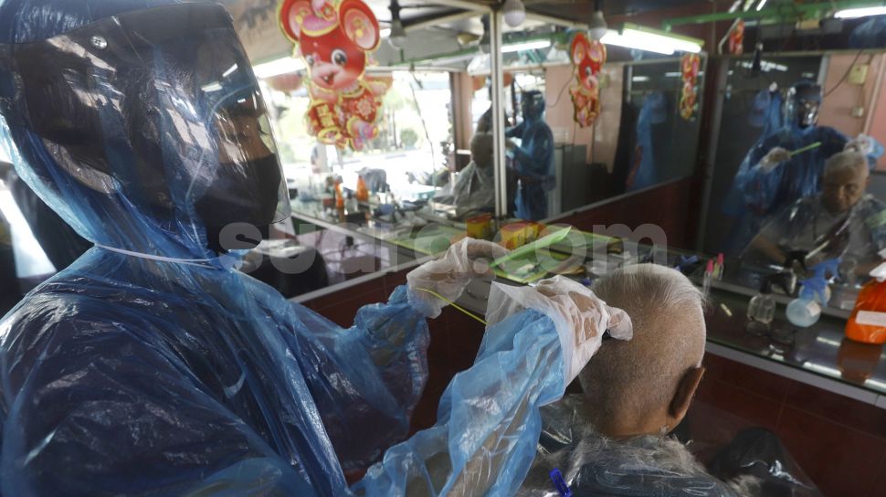 Tukang cukur menggunakan APD (Alat Pelindung Diri) saat mencukur pelanggan di kawasan Pondok Kelapa, Jakarta Timur, Selasa (5/5). Suara.com/Angga Budhiyanto]
