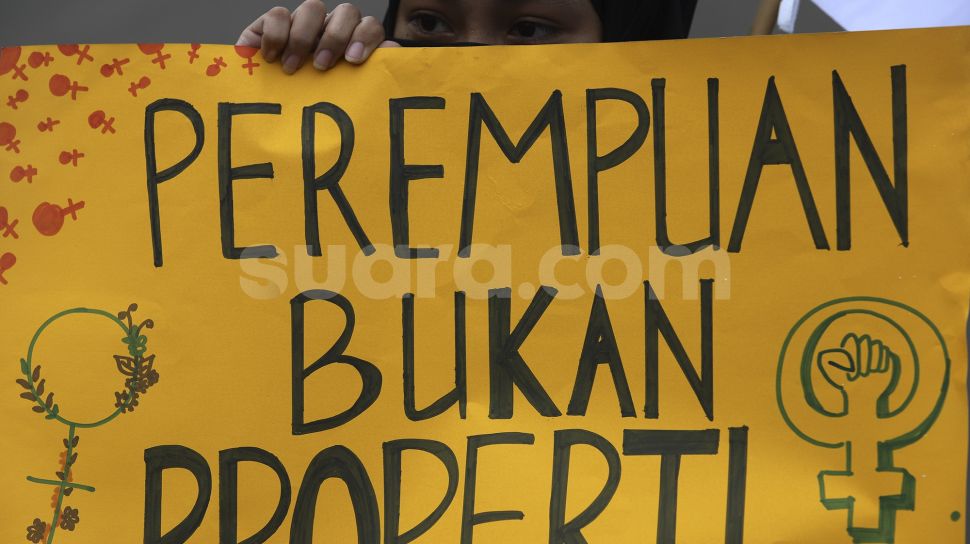 Seorang massa yang tergabung dalam Perempuan Mahardhika membawa poster saat melakukan aksi memperingati Hari Perempuan Internasional di kawasan Patung Kuda Arjuna Wiwaha, Jakarta, Senin (8/3/2021). [Suara.com/Angga Budhiyanto]